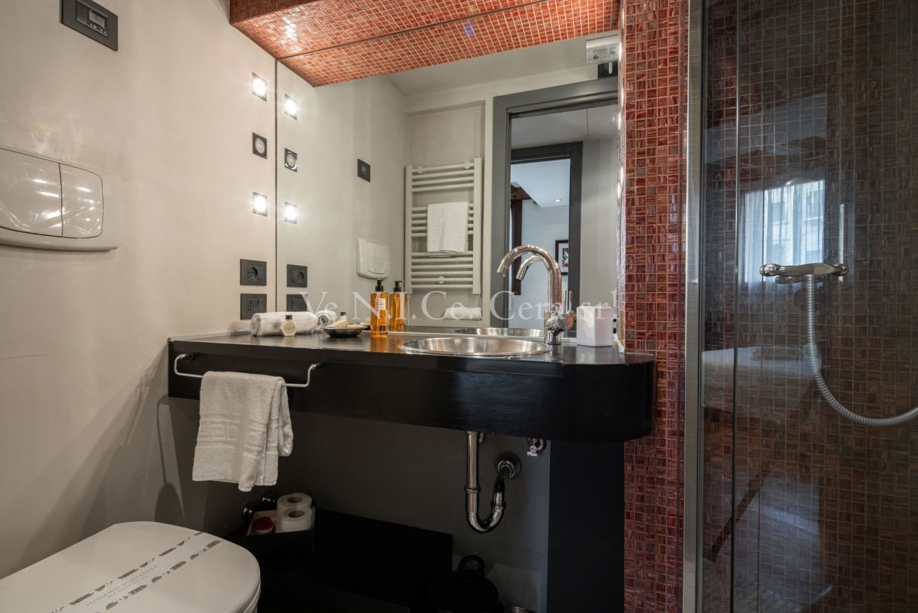 Een moderne badkamer met een zwart wastafel, spiegel, handdoekhouder en een douchecabine met glazen wanden.