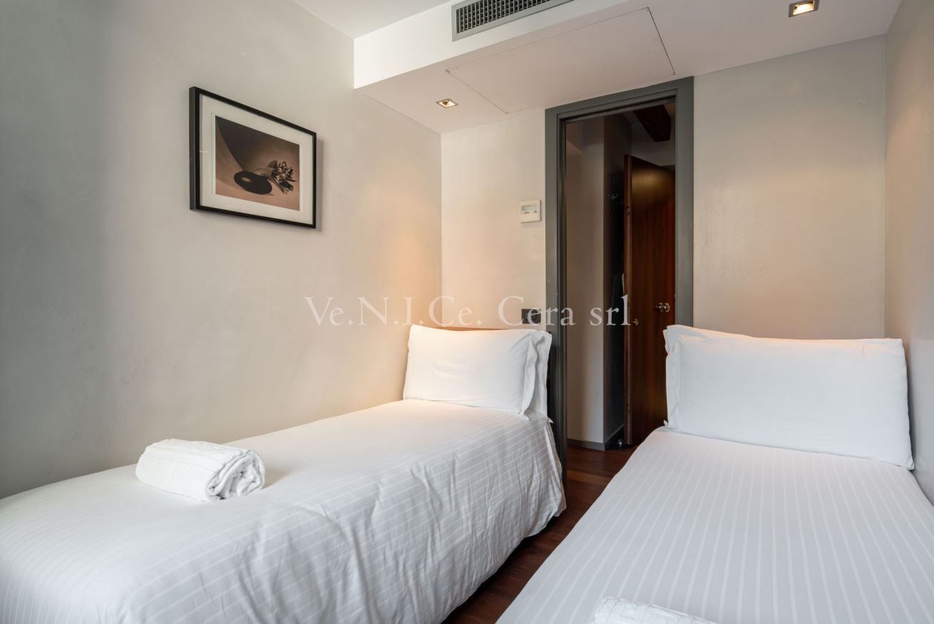 Une chambre d’hôtel avec deux lits, un tableau encadré au mur et une porte donnant sur une autre pièce.