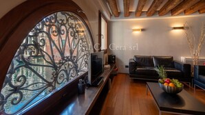 A modern living room with a large arched window, a black leather sofa, a wooden coffee table with fruit, and a TV on a wooden stand. - Ve.N.I.Ce. Cera San Moisè (Venezia)
