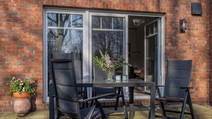 Une terrasse avec une table et des chaises, un pot de fleurs et un mur en briques.