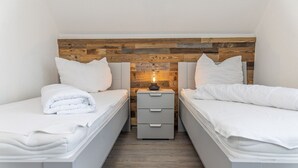 Une chambre double avec deux lits, une tête de lit en bois, une table de chevet avec une lampe et une petite commode.
