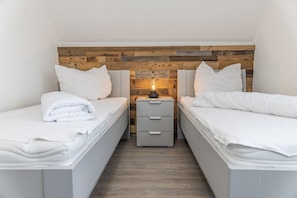 Habitación doble con dos camas, cabecero de madera, mesita de noche con lámpara y una pequeña cómoda.