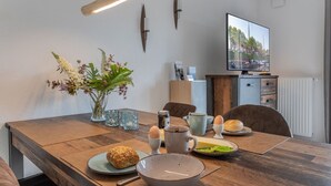 Un coin repas avec une table en bois, un vase de fleurs, un téléviseur et un radiateur.