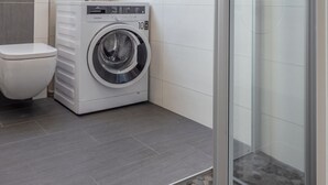 Une salle de bain moderne avec des toilettes blanches, un lave-linge à chargement frontal et un espace douche.