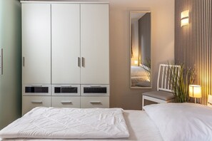 Une chambre avec une grande armoire, une table de chevet, un miroir et une lampe.