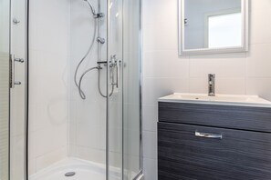 Une salle de bain moderne avec une douche à parois de verre, un meuble-lavabo en bois foncé et un miroir au-dessus du lavabo.