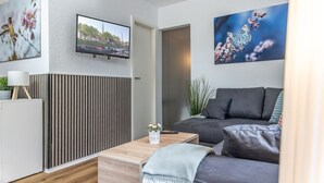 Un salon moderne avec un canapé gris, une table basse en bois et un téléviseur fixé au mur.