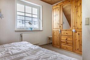 A bedroom with a bed, a window with a view, a wooden wardrobe, and a radiator. - Vacation home 50059 - Arrive in Altfunnixsiel and feel at home: Quiet (Wittmund)