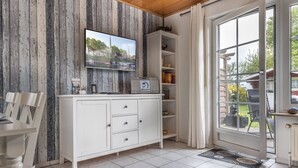 A kitchen with a white cabinet, a TV mounted on the wall, and a view of the outdoors through a glass door. - Vacation home 50059 - Arrive in Altfunnixsiel and feel at home: Quiet (Wittmund)