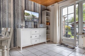 Ett kök med vita skåp, en tv som är monterad på väggen och utsikt över utomhusmiljön genom en glasdörr.