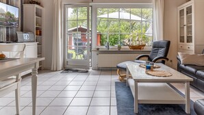 A modern living room with a dining table, a sofa, a TV, and a grill. - Vacation home 50059 - Arrive in Altfunnixsiel and feel at home: Quiet (Wittmund)