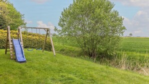 A playground with a slide and swings, surrounded by grass and trees. - Vacation home 50059 - Arrive in Altfunnixsiel and feel at home: Quiet (Wittmund)