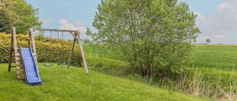 A playground with a slide and swings, surrounded by grass and trees.