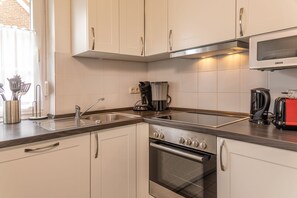 A modern kitchen with white cabinets, a stainless steel stove, a microwave, and a coffee maker. - Vacation home 50007 - pure comfort and relaxation: the semi-detached house with (Wittmund)