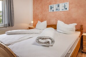 A neatly made bed with white linens and pillows, a wooden headboard, a nightstand with a lamp, and a wall with framed artwork. - 50012 Holiday apartment "Svenja" - Holiday apartment "Svenja": Bright upper floor apartment (Wittmund)