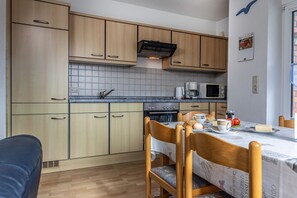 A compact kitchen with wooden cabinets, a tiled backsplash, a microwave, a coffee maker, and a dining table set for breakfast. - 50012 Holiday apartment "Svenja" - Holiday apartment "Svenja": Bright upper floor apartment (Wittmund)