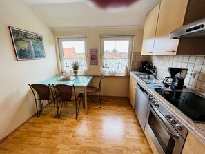 Una cocina compacta con una mesa de comedor, sillas, estufa y ventana con vistas a edificios.