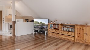 Una cocina moderna con horno empotrado, una zona de comedor con mesa y sillas, y un armario de madera con libros.