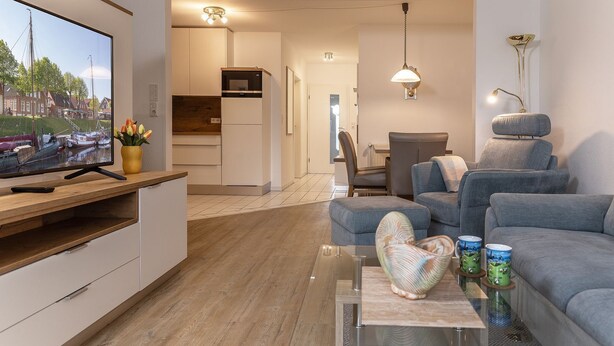 A modern living room with a flat-screen TV, grey sofas, a glass coffee table, and a view of a canal. - Open and flooded with light: the first floor apartment with its 62 square meters was brightly (Wittmund)