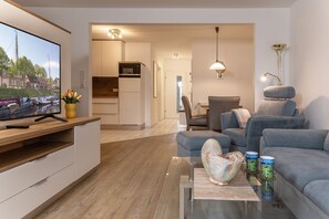 A modern living room with a flat-screen TV, grey sofas, a glass coffee table, and a view of a canal. - Open and flooded with light: the first floor apartment with its 62 square meters was brightly (Wittmund)