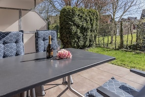 Un patio esterno con tavolo, cuscini, una bottiglia di vino e un bicchiere.