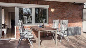 Un patio al aire libre con una mesa y sillas, un muro de ladrillo y una puerta corrediza de vidrio que da a un espacio interior.