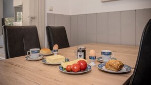 Una mesa de comedor con platos de comida, entre ellos huevos, pan y tomates, y dos tazas con sus platillos.
