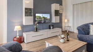 Una sala de estar moderna con un televisor de pantalla plana, muebles blancos, un reloj y un sofá azul.