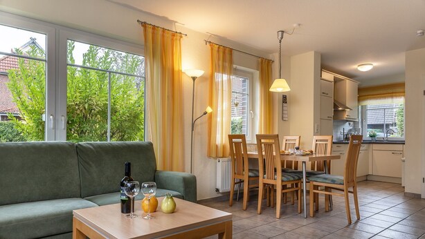 Ein gemütliches Wohnzimmer mit einer Couch, einem Esstisch mit Stühlen und einem durchgehenden offenen Durchgang zur Küche.