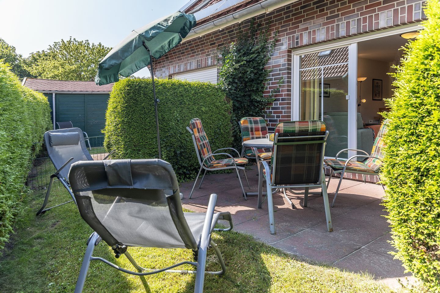 Eine Terrasse mit Tisch und Stühlen, ein Liegestuhl und ein grüner Sonnenschirm.