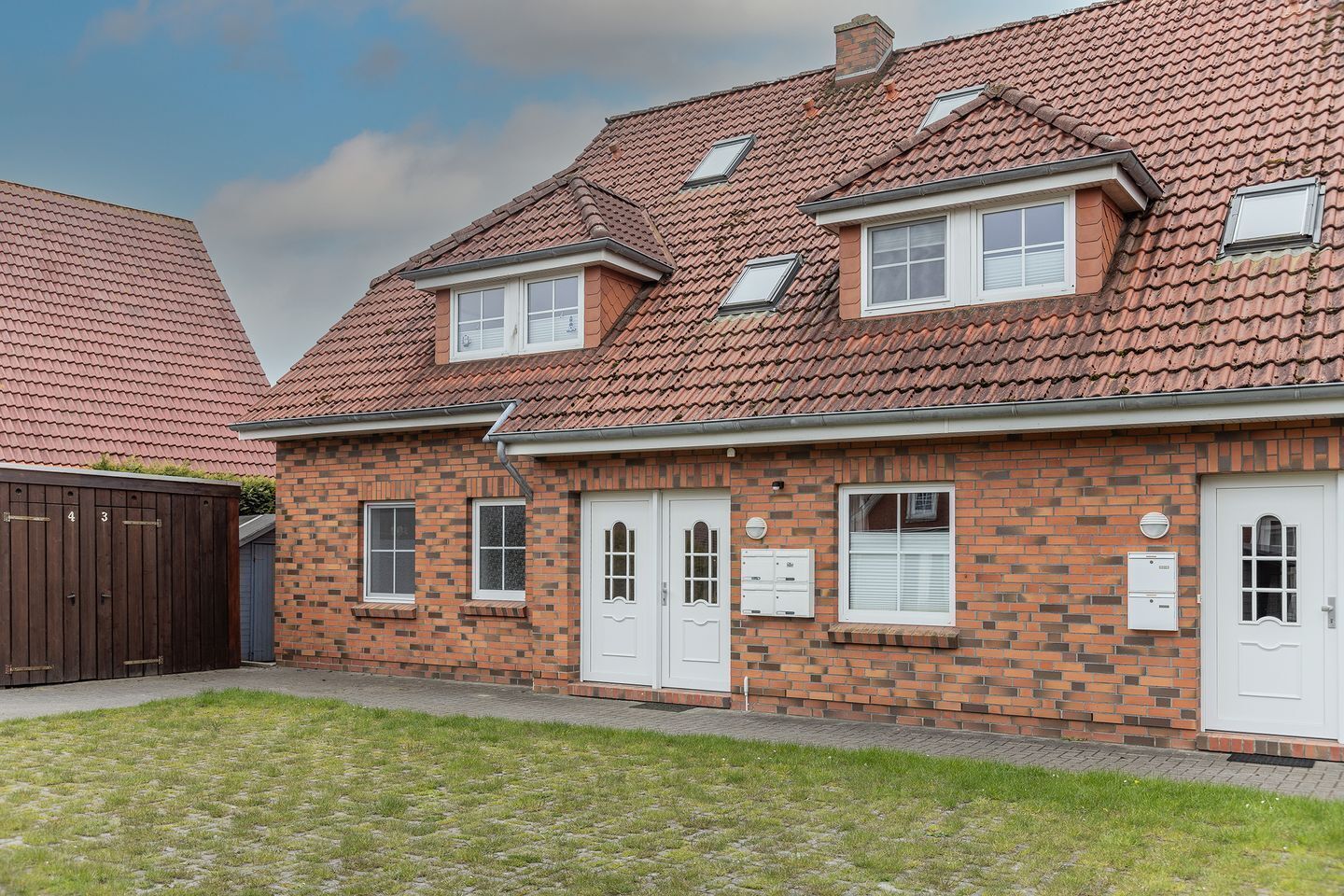 A two-story brick house with a red-tiled roof, white doors, and multiple windows.