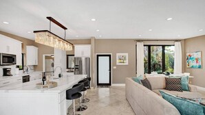 A modern kitchen with white cabinetry, a central island with bar stools, and a dining area with a sofa and cushions. - Private Waterfront Home in Wilton Manors - Dock & BBQ - Minutes From The Beach (Wilton Manors)