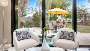 A modern living room with two white armchairs, a glass coffee table, and a yellow umbrella outside. - Private Waterfront Home in Wilton Manors - Dock & BBQ - Minutes From The Beach (Wilton Manors)
