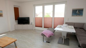 A modern living room with a TV, a dining table, a sofa, and a bench. - Bright and open: The homely apartment, which was completed in 2017 (Wittmund)