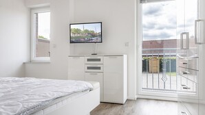 A bedroom with a bed, a TV mounted on a cabinet, and a sliding glass door leading to a balcony.