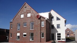 A two-story residential building with a brick facade and white upper section, featuring multiple windows and a satellite dish.