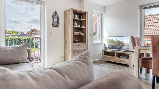 A modern living room with a sofa, a wooden bookshelf, a TV, and a dining area with a table and chairs.