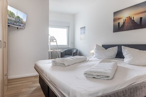 Habitación de hotel con cama, escritorio, silla, ventana y un cuadro en la pared.