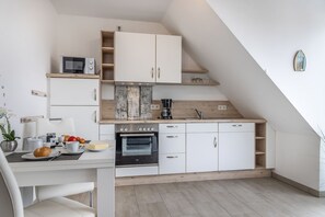 Una cocina compacta con microondas, horno y cafetera, un comedor con mesa y sillas, y un techo inclinado.