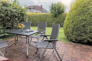 Eine Terrasse im Freien mit Tisch und Stühlen, einer Vase mit Blumen und einem gepflegten Heckenabschnitt.