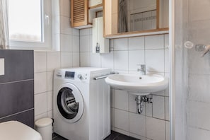 Une petite buanderie équipée d’un lave-linge à chargement frontal, d’un évier et de toilettes.