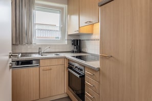 Eine Küche mit Holzschränken, einer Edelstahlspüle, einem Einbauofen und einem Fenster mit Vorhängen.