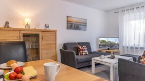 Ein modernes Wohnzimmer mit einem Holzespeisetisch, grauen Sofas, einem Flachbildfernseher und einem Gemälde an der Wand.