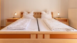 Ein Doppelbett mit zwei Nachttischen, jeweils mit einer Lampe, in einem Zimmer mit einem Holz-Kopfteil und einer Heizung.