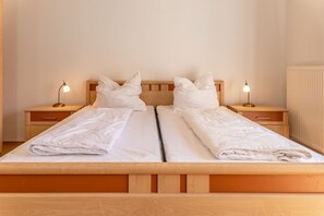 Ein Doppelbett mit zwei Nachttischen, jeweils mit einer Lampe, in einem Zimmer mit einem Holz-Kopfteil und einer Heizung.