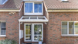 Ein zweigeschossiges Backsteinhaus mit einem zentralen Eingang, einer kleinen Veranda und einem Fenster mit Blick auf den Garten.