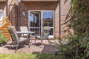 Eine Terrasse mit Tisch und Stühlen, eine Holztreppe und ein Backsteinhaus mit Glastür.