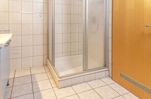 Ein Badezimmer mit Dusche, gefliesten Wänden, einem Waschbecken und einer Holztür.