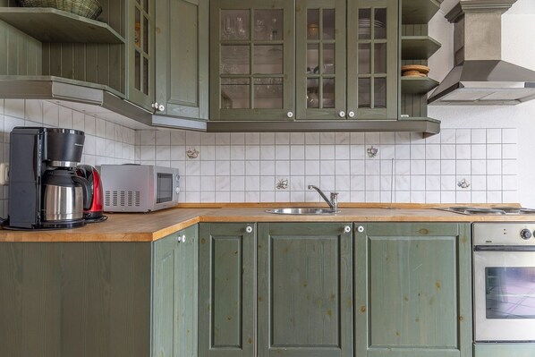 Una cocina con armarios verdes, cafetera, microondas y estufa.