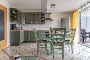 A kitchen with green cabinets, a microwave, a coffee maker, and a dining area with two chairs.
